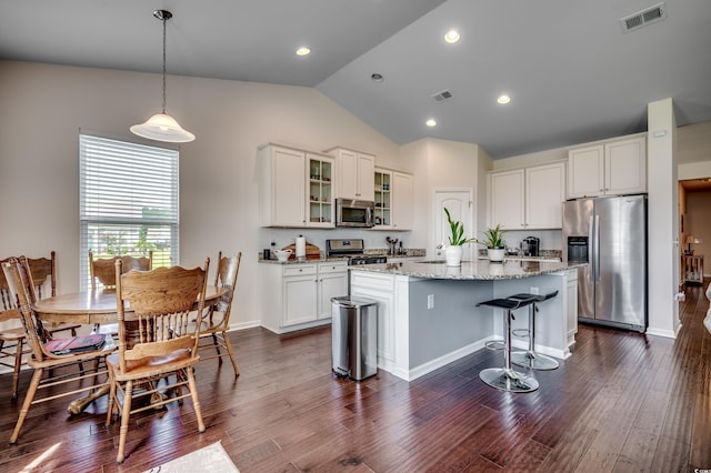 kitchen with light stone counters, stainless steel appliances, vaulted ceiling, dark hardwood / wood-style floors, and an island with sink