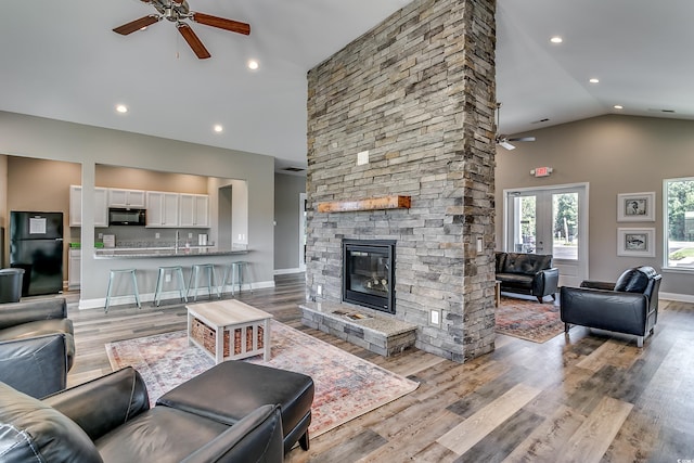 living room featuring ceiling fan, a stone fireplace, high vaulted ceiling, and light hardwood / wood-style flooring