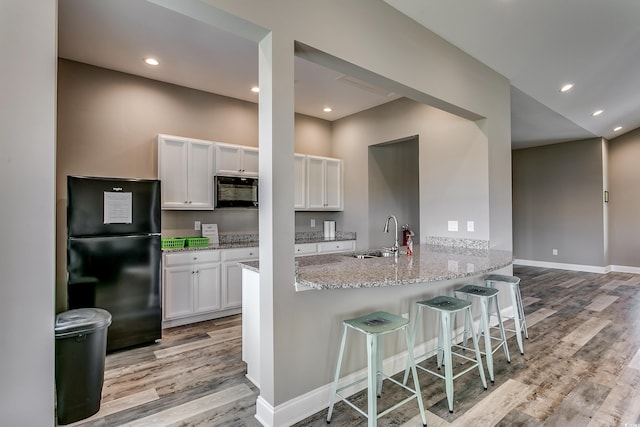 kitchen featuring white cabinetry, sink, kitchen peninsula, black appliances, and light wood-type flooring