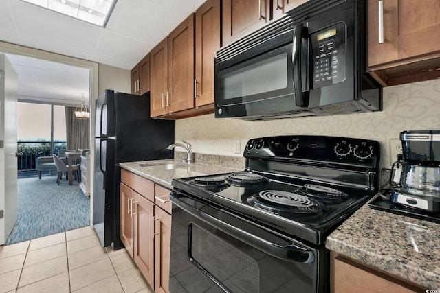 kitchen with light stone counters, sink, black appliances, light tile patterned floors, and a notable chandelier