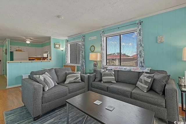 living room with wood-type flooring, a textured ceiling, ceiling fan, and ornamental molding