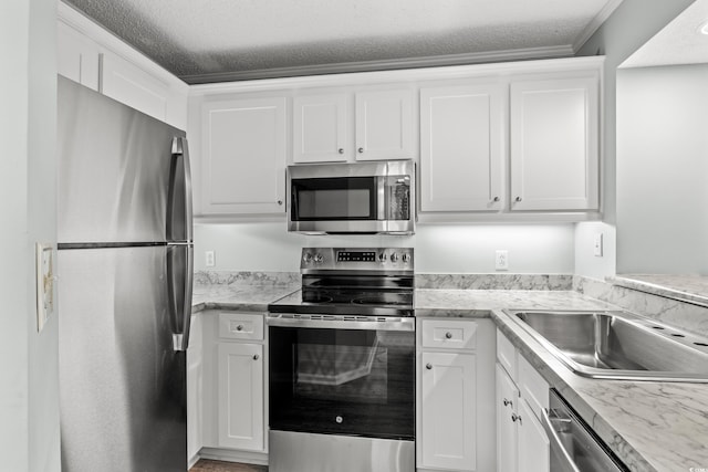 kitchen featuring white cabinets, ornamental molding, a textured ceiling, and appliances with stainless steel finishes