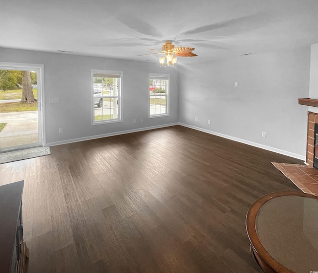 unfurnished living room with a fireplace, ceiling fan, dark hardwood / wood-style flooring, and a healthy amount of sunlight