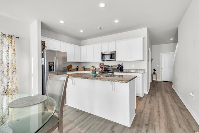 kitchen with white cabinets, dark stone countertops, an island with sink, and appliances with stainless steel finishes