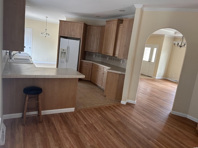 kitchen featuring sink, light hardwood / wood-style flooring, backsplash, white refrigerator with ice dispenser, and kitchen peninsula