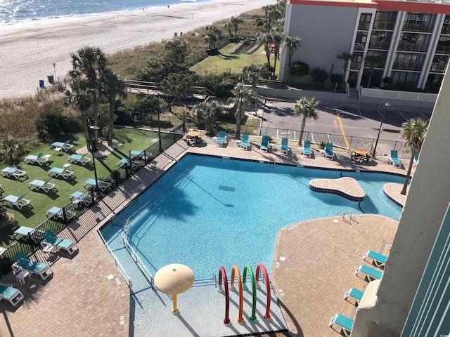 view of swimming pool featuring a view of the beach, a patio, and a water view