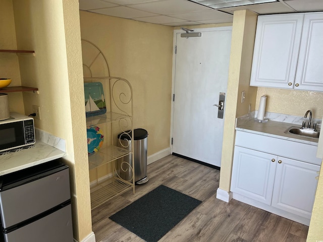 kitchen with white cabinets, a paneled ceiling, light wood-type flooring, and sink