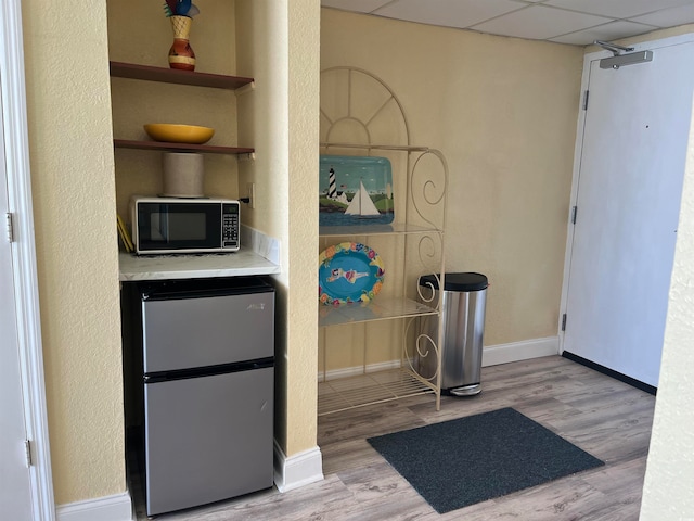 kitchen with a paneled ceiling, light wood-type flooring, and stainless steel refrigerator