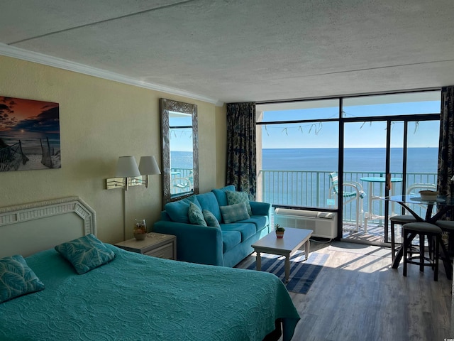 bedroom featuring a wall mounted air conditioner, a water view, crown molding, hardwood / wood-style flooring, and a textured ceiling