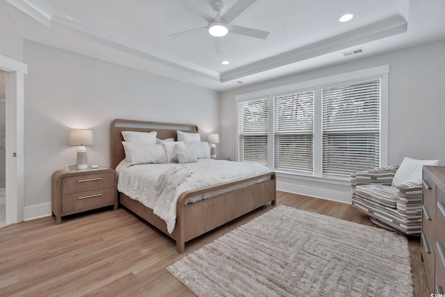 bedroom featuring ceiling fan, light hardwood / wood-style flooring, and a tray ceiling