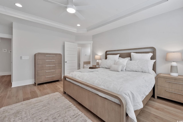 bedroom with ceiling fan, light wood-type flooring, and a tray ceiling