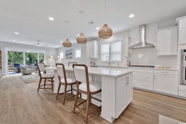 kitchen featuring a kitchen island, wall chimney range hood, white cabinetry, and light hardwood / wood-style flooring