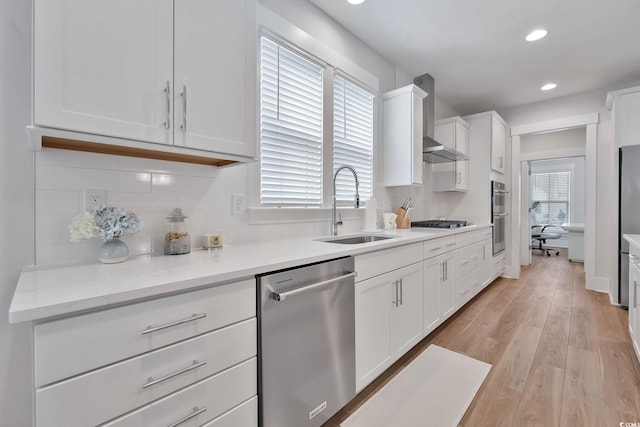 kitchen featuring sink, wall chimney exhaust hood, a healthy amount of sunlight, white cabinets, and appliances with stainless steel finishes