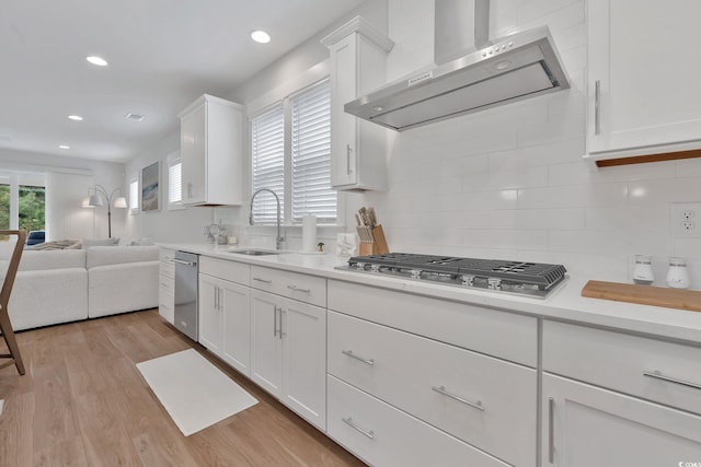 kitchen with light wood-type flooring, tasteful backsplash, wall chimney exhaust hood, stainless steel gas cooktop, and white cabinets