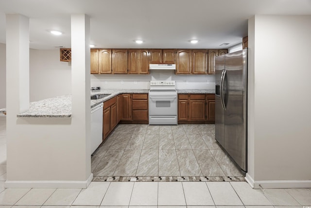 kitchen with light tile patterned flooring, white appliances, light stone countertops, and sink