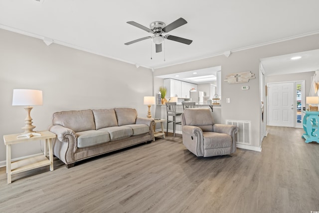 living room featuring ceiling fan, ornamental molding, and light wood-type flooring