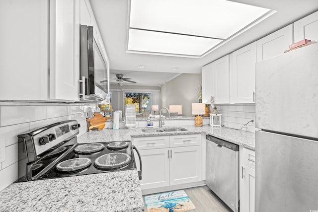 kitchen with sink, stainless steel appliances, light stone countertops, decorative backsplash, and white cabinets