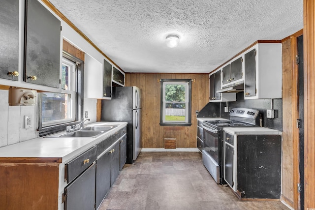 kitchen featuring a textured ceiling, wooden walls, sink, stainless steel refrigerator, and range with electric stovetop