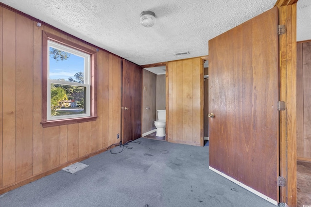 corridor featuring a textured ceiling, dark carpet, and wooden walls