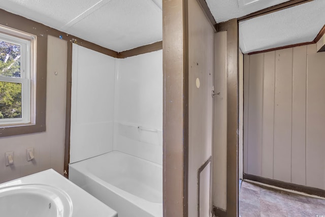 bathroom with shower / bathing tub combination, sink, a textured ceiling, and wooden walls