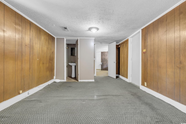 unfurnished room with a textured ceiling, wood walls, and sink