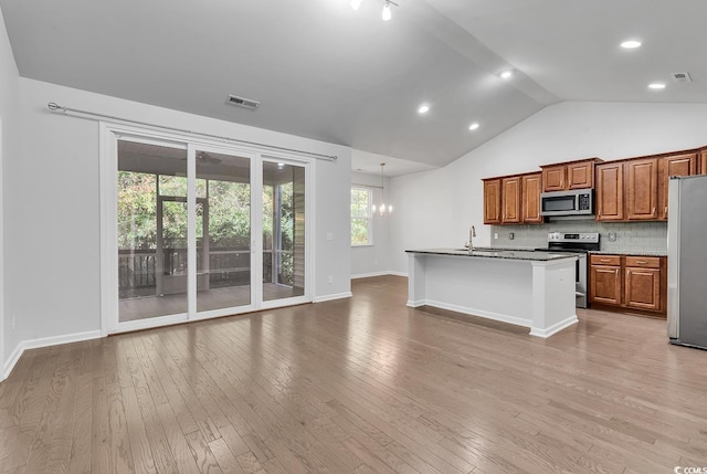 kitchen with appliances with stainless steel finishes, a center island with sink, lofted ceiling, and light hardwood / wood-style floors