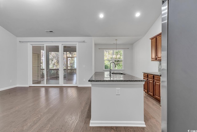 kitchen with a kitchen island with sink, dark wood-type flooring, sink, dark stone countertops, and lofted ceiling