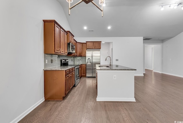 kitchen with lofted ceiling, a kitchen island with sink, light stone countertops, wood-type flooring, and stainless steel appliances