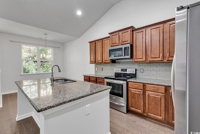 kitchen with sink, light hardwood / wood-style floors, lofted ceiling, a kitchen island with sink, and appliances with stainless steel finishes