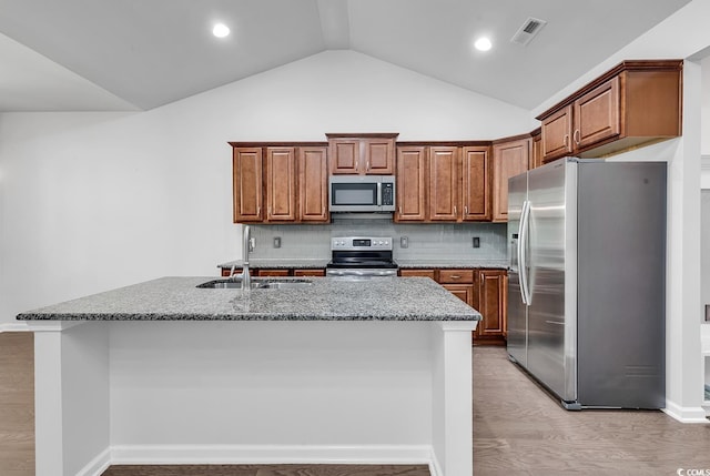 kitchen with appliances with stainless steel finishes, vaulted ceiling, sink, light hardwood / wood-style floors, and an island with sink