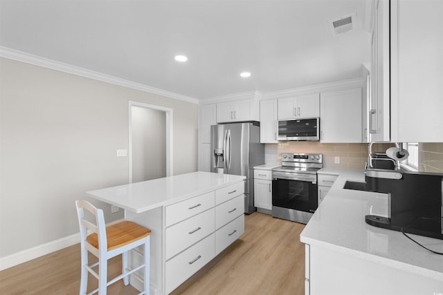 kitchen with white cabinets, light hardwood / wood-style flooring, a kitchen island, and appliances with stainless steel finishes