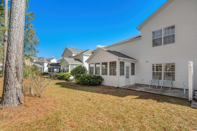 back of property featuring a sunroom, a patio area, and a lawn