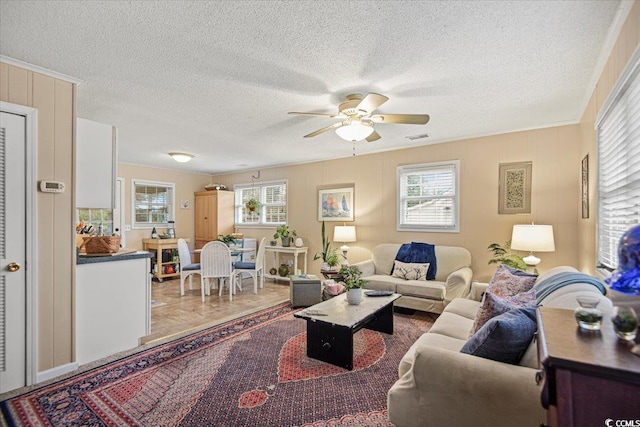 tiled living room with ornamental molding, a textured ceiling, ceiling fan, and a healthy amount of sunlight