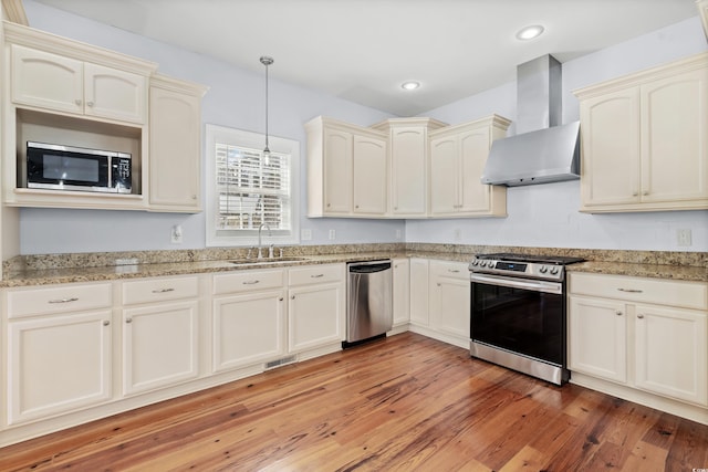 kitchen featuring wall chimney exhaust hood, stainless steel appliances, sink, light hardwood / wood-style flooring, and hanging light fixtures