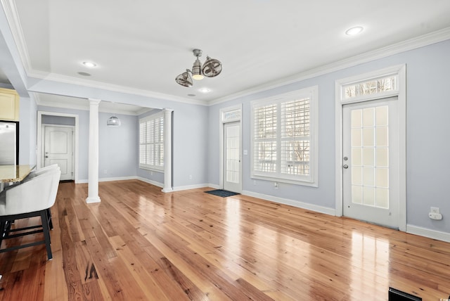 interior space with light hardwood / wood-style flooring, a notable chandelier, crown molding, and ornate columns