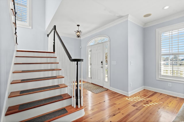 foyer entrance with light wood-type flooring, crown molding, a healthy amount of sunlight, and a notable chandelier