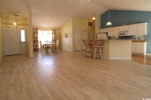 unfurnished living room with ceiling fan with notable chandelier, light wood-type flooring, and high vaulted ceiling