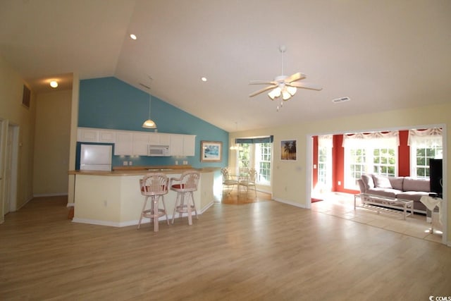 kitchen featuring white appliances, high vaulted ceiling, light hardwood / wood-style flooring, white cabinetry, and a breakfast bar area