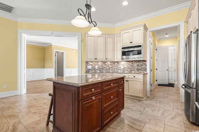 kitchen featuring decorative light fixtures, a center island, light stone counters, stainless steel appliances, and cream cabinetry