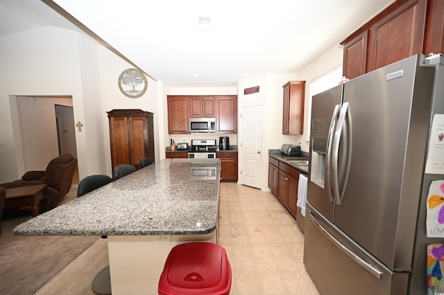 kitchen featuring a kitchen island, appliances with stainless steel finishes, a breakfast bar, and dark stone counters