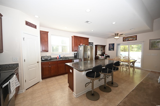 kitchen featuring a kitchen bar, sink, appliances with stainless steel finishes, a kitchen island, and dark stone counters