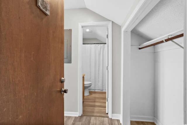 bathroom featuring toilet, wood-type flooring, electric panel, and vaulted ceiling