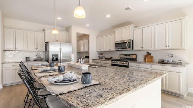 kitchen featuring pendant lighting, an island with sink, stainless steel appliances, and light wood-type flooring