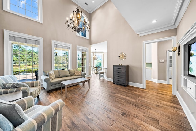 living room with a chandelier, hardwood / wood-style floors, crown molding, and a high ceiling