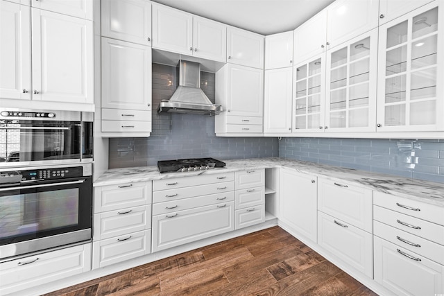 kitchen featuring light stone countertops, appliances with stainless steel finishes, wall chimney range hood, white cabinets, and dark hardwood / wood-style floors