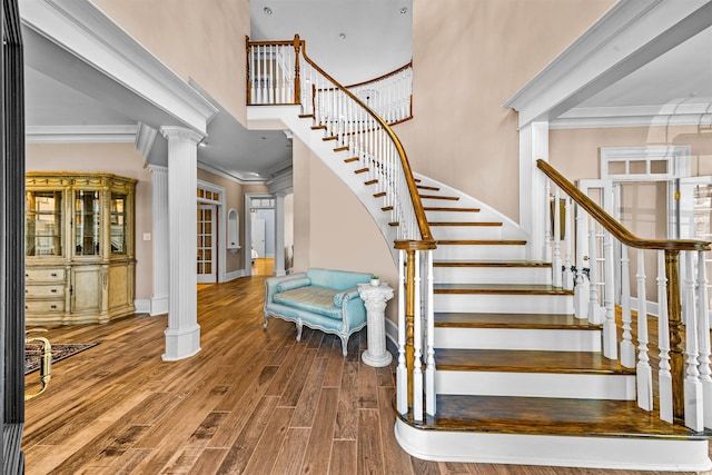 staircase with decorative columns, crown molding, hardwood / wood-style floors, and a high ceiling