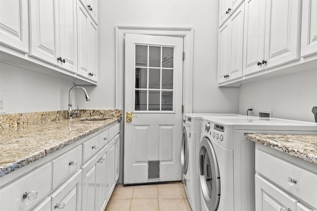 clothes washing area with washer and clothes dryer, sink, light tile patterned floors, and cabinets