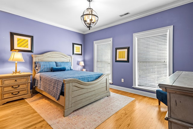 bedroom with light hardwood / wood-style floors, an inviting chandelier, multiple windows, and ornamental molding