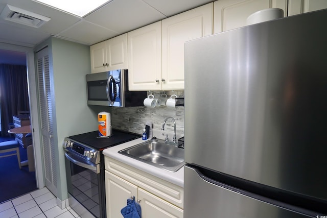 kitchen with a drop ceiling, backsplash, white cabinets, sink, and appliances with stainless steel finishes