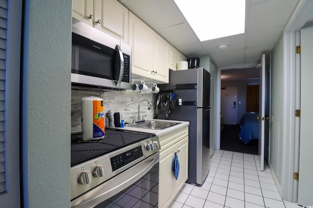 kitchen featuring decorative backsplash, appliances with stainless steel finishes, sink, light tile patterned floors, and white cabinetry